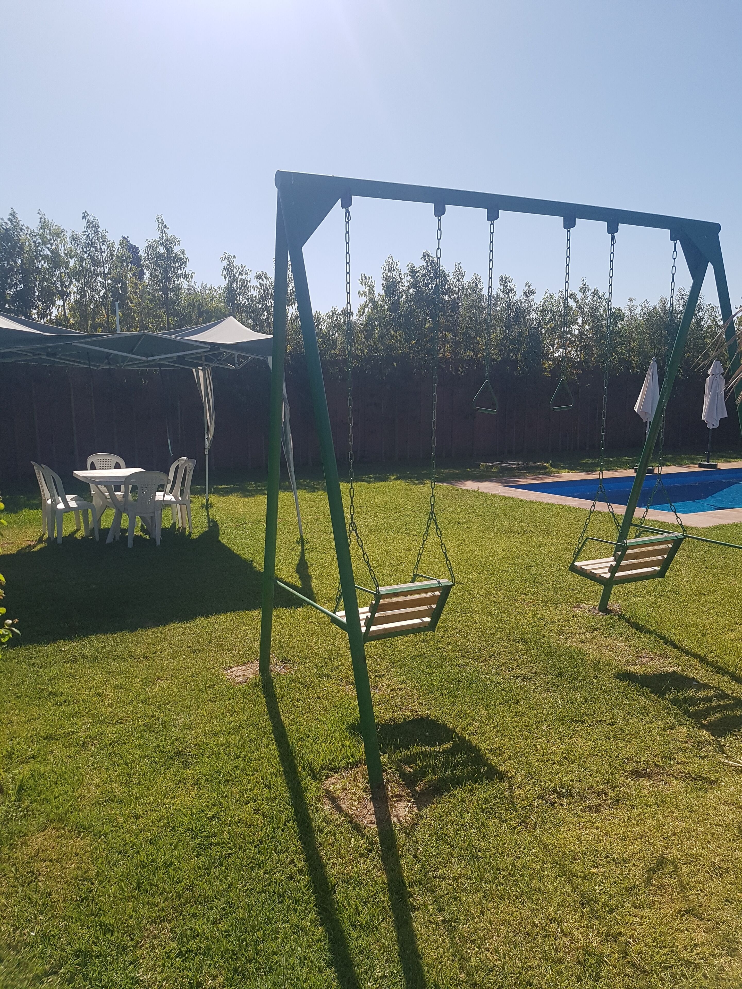 En baghave med gyngestativ, overdækket bord med stole og en swimmingpool.