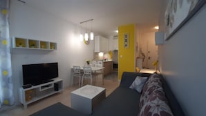 A modern living room with a flat-screen TV, a sofa, a coffee table, and a dining area with a table and chairs.