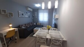 A modern living room with a sofa, a dining table with chairs, a desk with a lamp, and artwork on the walls. - Verdi 1-bed Apartment in Split (Split)