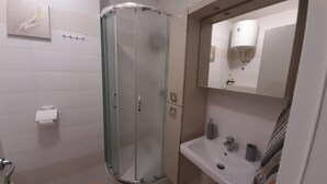 A modern bathroom with a glass shower enclosure, a white sink with a mirror above it, and a towel rack on the wall.