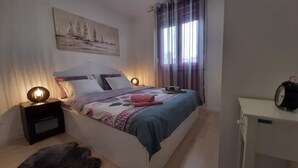 A bedroom with a bed, two bedside tables, a nightstand, a desk, and a chair.