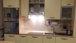 A compact kitchen with a sink, two ovens, a microwave, and a dining area with a chair. - Iseolake 1-bed Apartment in Provaglio D'iseo (Provaglio d'Iseo)
