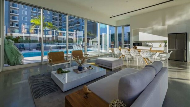 A modern living room with a large glass wall, a pool, and a kitchen area.