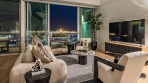 Un salon moderne doté d’un grand téléviseur, de sièges confortables, d’une table basse et offrant une vue sur le paysage urbain illuminé la nuit.