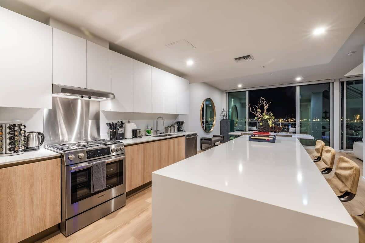 A modern kitchen with stainless steel appliances, a large island, and a view of the city at night.