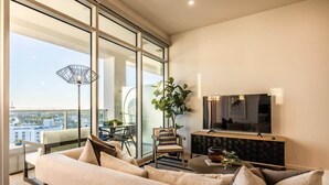A modern living room with a sofa, a TV, and a dining area with chairs and a table. - @ Marbella Lane - Luxury Beachside 2BR (Long Beach)