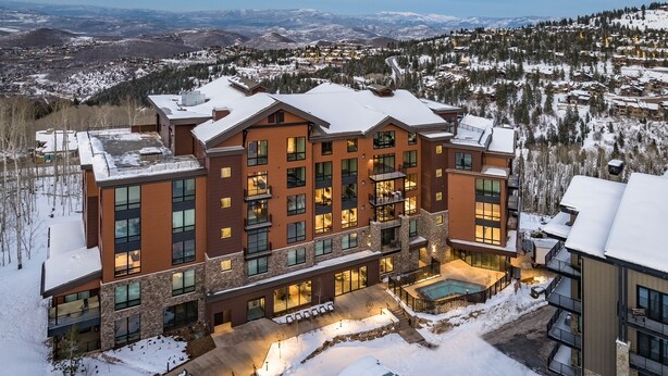 A modern multi-story building with a snow-covered roof, large windows, and a pool area. - Luxe Deer Valley Ski-In/Out. 50 ft to Lift. Bowling Alley, Hot Tub & Ski Valet (Park City)