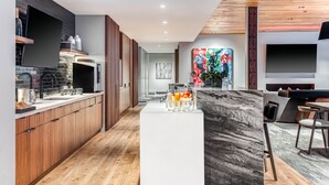 A modern kitchen with wooden cabinets, a marble island, and a dining area with a TV and seating. - Luxe Deer Valley Ski-In/Out. 50 ft to Lift. Bowling Alley, Hot Tub & Ski Valet (Park City)