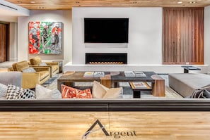 A modern living room with a fireplace, comfortable seating, a large TV, and a colorful abstract painting.