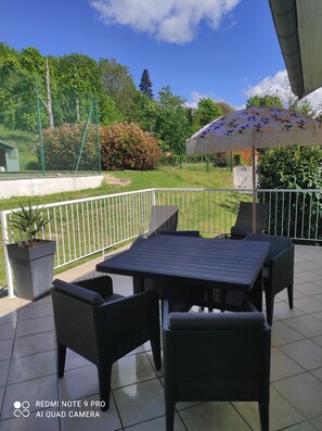 Relax in a serene outdoor space with a table and chairs, surrounded by lush greenery and a shaded area.