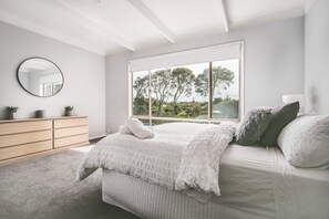 Relax in a serene space with a large bed, dresser, and window overlooking lush trees.