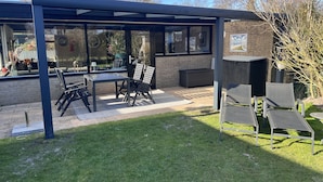 Patio esterno con struttura in vetro, tavolo e sedie.