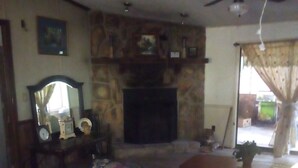 Uma sala de estar com sofá, lareira, ventilador de teto e janela com cortinas.