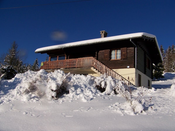 Une cabane en bois dotée d’un balcon, entourée d’arbres couverts de neige.