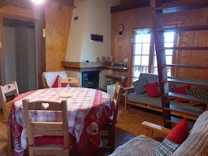 L’intérieur chaleureux d’un chalet avec une table à manger en bois, des chaises, un canapé et une cheminée.