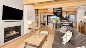 Ein modernes Wohnzimmer mit Kamin, Holzboden, einer Couch und einer Wendeltreppe.