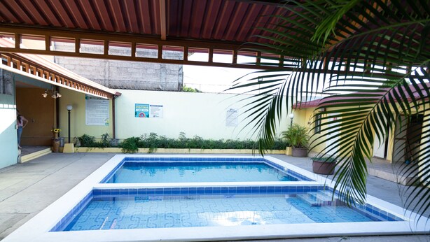Piscina retangular com azulejos azuis, rodeada por um deck de concreto e plantas em vasos.