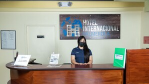 Bancada de recepção do Hotel Internacional Palmerola com acabamento em madeira, uma placa indicando o nome do hotel acima e uma placa na parede à esquerda.
