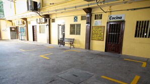 Entrada de hotel com um banco, uma placa com o nome 'Cocina' e uma tampa de bueiro no pavimento.