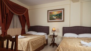 Quarto de hotel com duas camas, uma mesinha, uma cadeira, um abajur e um quadro na parede.