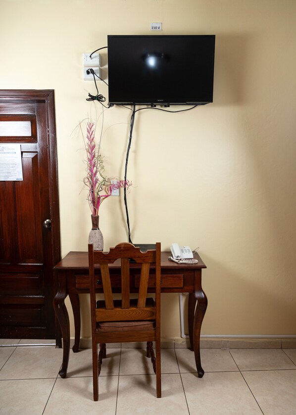 Un escritorio de madera con una silla, un teléfono y un televisor fijado a la pared.