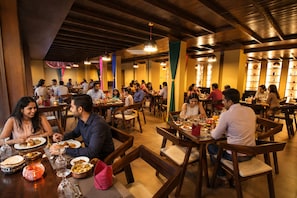 Un restaurant avec des tables et des chaises en bois, des clients qui déjeunent ou dînent, et une ambiance chaleureuse.
