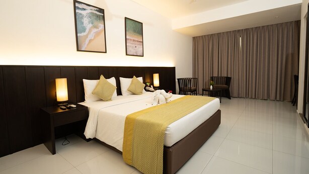 A hotel room with a large bed, a nightstand, a desk, a chair, and a TV. - KYNROCK Airport Hotel (Seeduwa - Katunayake)
