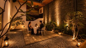 Un espace extérieur aménagé pour les repas, avec un mur en pierre, un sol carrelé et des plantes en pot.