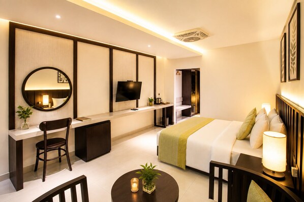 Una habitación de hotel moderna con cama, escritorio, silla, televisión y un espejo redondo.