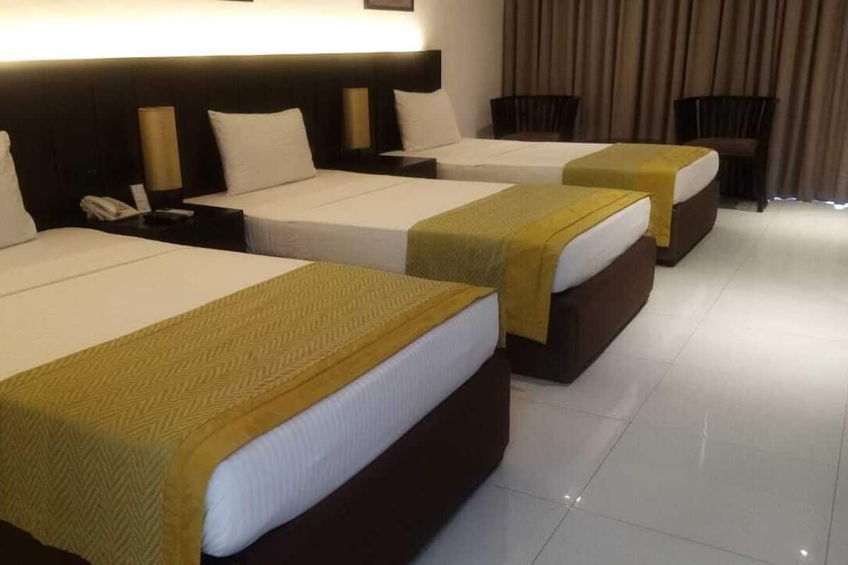 A hotel room with three beds, each with a white mattress and a brown headboard.