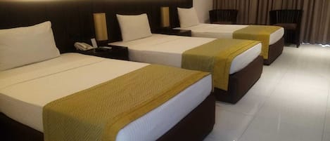 A hotel room with three beds, each with a white mattress and a brown headboard.