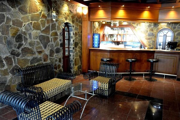 Un espace bar avec des murs en pierre, une table en verre et des tabourets de bar noirs.