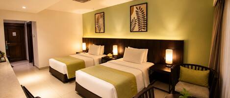A hotel room with two beds, a dining table, a chair, a small table with a candle, and a door.