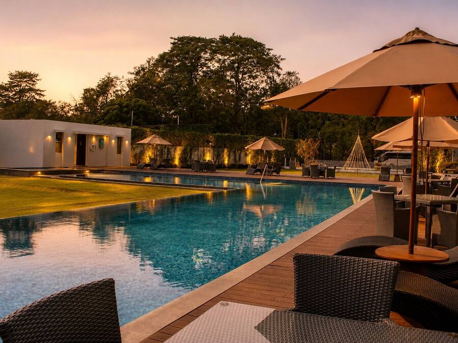 A swimming pool with lounge chairs and umbrellas, surrounded by a landscaped garden and a building with outdoor lighting.
