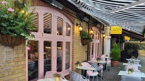 An outdoor cafe with pink-framed windows, tables with chairs, and a canopy. - Charming Baby Narrowboat Apsley Marina (Hemel Hempstead)