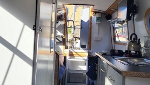 A narrow, well-lit kitchen with a sink, stove, and a small window. - Charming Baby Narrowboat Apsley Marina (Hemel Hempstead)