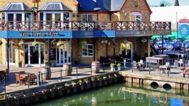 A waterfront building with a sign reading "The Paper Mill." It features a brick facade, a covered patio area, and a small canal in front. - Charming Baby Narrowboat Apsley Marina (Hemel Hempstead)