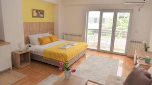 A bedroom with a bed, a bedside table, a nightstand, a window, and a view of the outside. - Unique Apartment Leninova (Skopje)