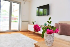 Ein Wohnzimmer mit einer weißen, strukturierten Vase auf einem Holztisch, gefüllt mit rosa Rosen.