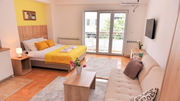 A modern hotel room with a bed, a sofa, a coffee table, and a TV. - Unique Apartment Leninova (Skopje)