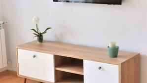 A modern living room with a wooden TV stand, a flat-screen TV mounted on the wall, and a small potted plant on the stand. - Unique Apartment Leninova (Skopje)