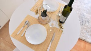 A round dining table with white plates, cutlery, and a bottle of wine. - Unique Apartment Leninova (Skopje)