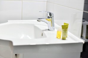 Ein weißes Waschbecken mit chromfarbenem Wasserhahn und einer gelben Lotionflasche auf der Ablagefläche.