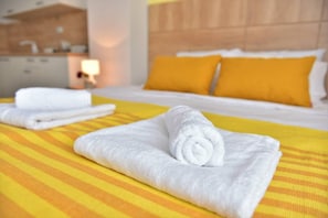 A hotel room with a bed, two rolled towels, and a yellow-striped bedspread.