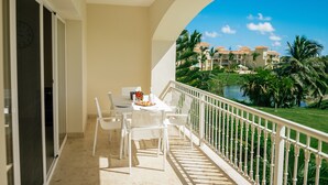 A balcony with a table set for two, overlooking a pool and resort buildings. - Special offer for amazing apartment in Bavaro with the Wi-Fi, pool and security. (Bavaro)