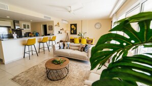 A modern kitchen with a built-in oven, a dining area with yellow chairs, a beige sofa, and a coffee table with flowers. - Special offer for amazing apartment in Bavaro with the Wi-Fi, pool and security. (Bavaro)