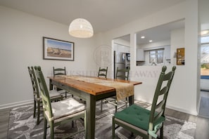 A dining area with a wooden table, green upholstered chairs, a patterned rug, and a hanging light fixture.