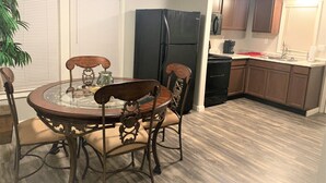 A dining area with a glass-top table and wooden chairs, a black refrigerator, and wooden cabinets in a kitchen.