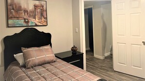 A bedroom with a bed, a nightstand, a painting, and a white door.