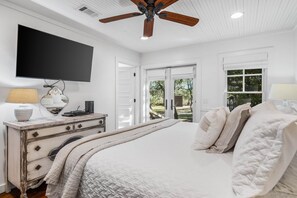 Quarto com cama grande, ventilador de teto, televisão de tela plana, cômoda e janela com vista para o exterior.